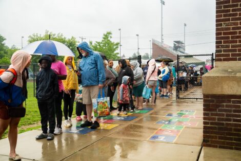Community members line up in the rain with umbrellas to get ready for the West Ward Sale.